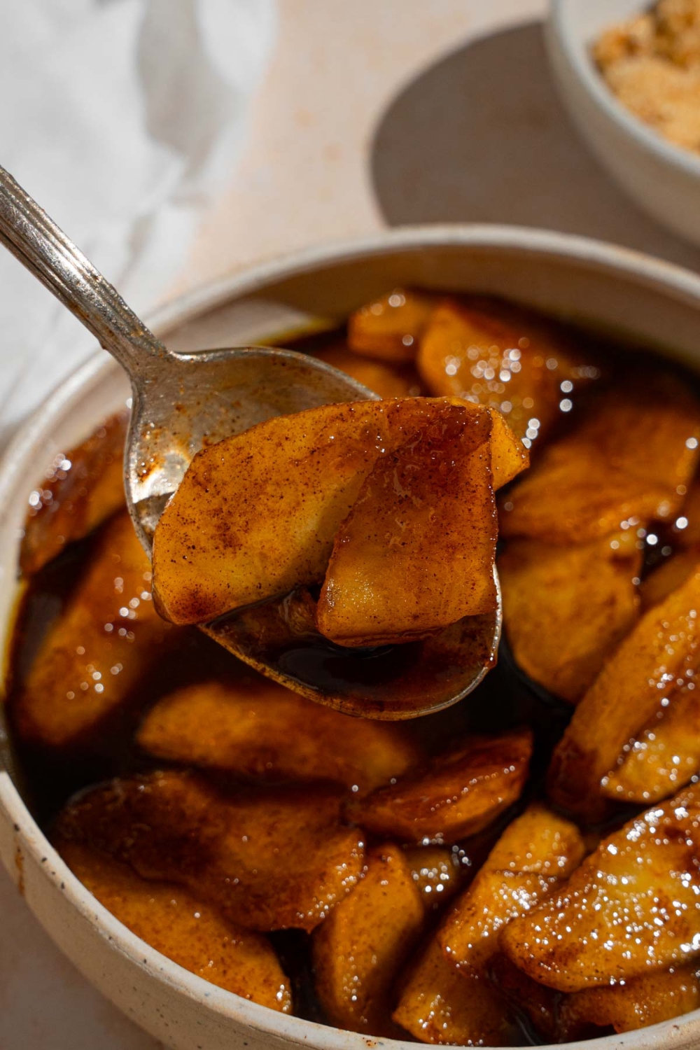 A bowl of copycat Cracker Barrel fried apples with a spoon taking a bite of apples. The bowl is on a tan counter with a white cloth napkin.