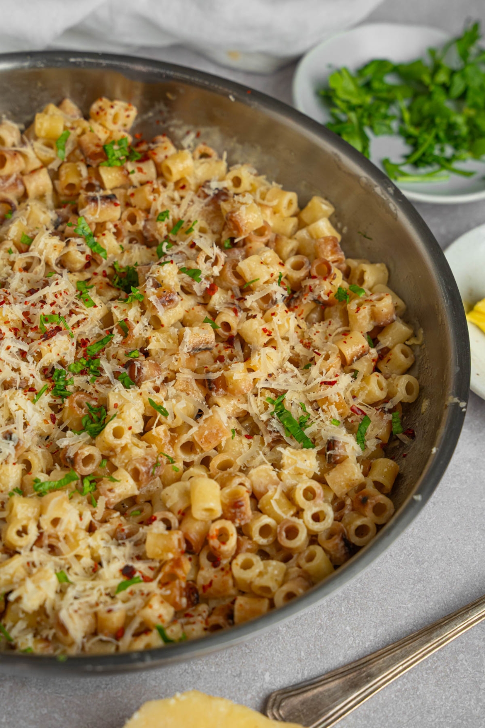 A pan with ditalini pasta garnished with fresh parsley and grated cheese. The pan is on a white counter with a ramekin of fresh parsley.