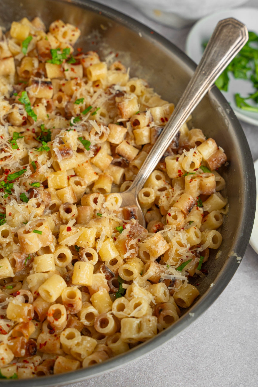 A skillet with ditalini pasta garnished with fresh parsley and grated cheese. There is a spoon in the pasta.