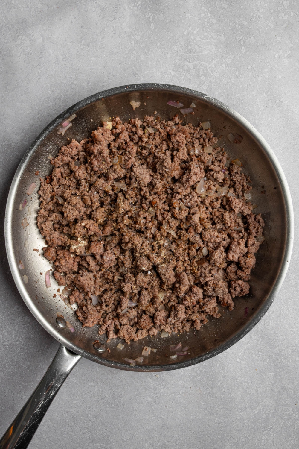A skillet with browned ground beef. The skillet is on a white counter.