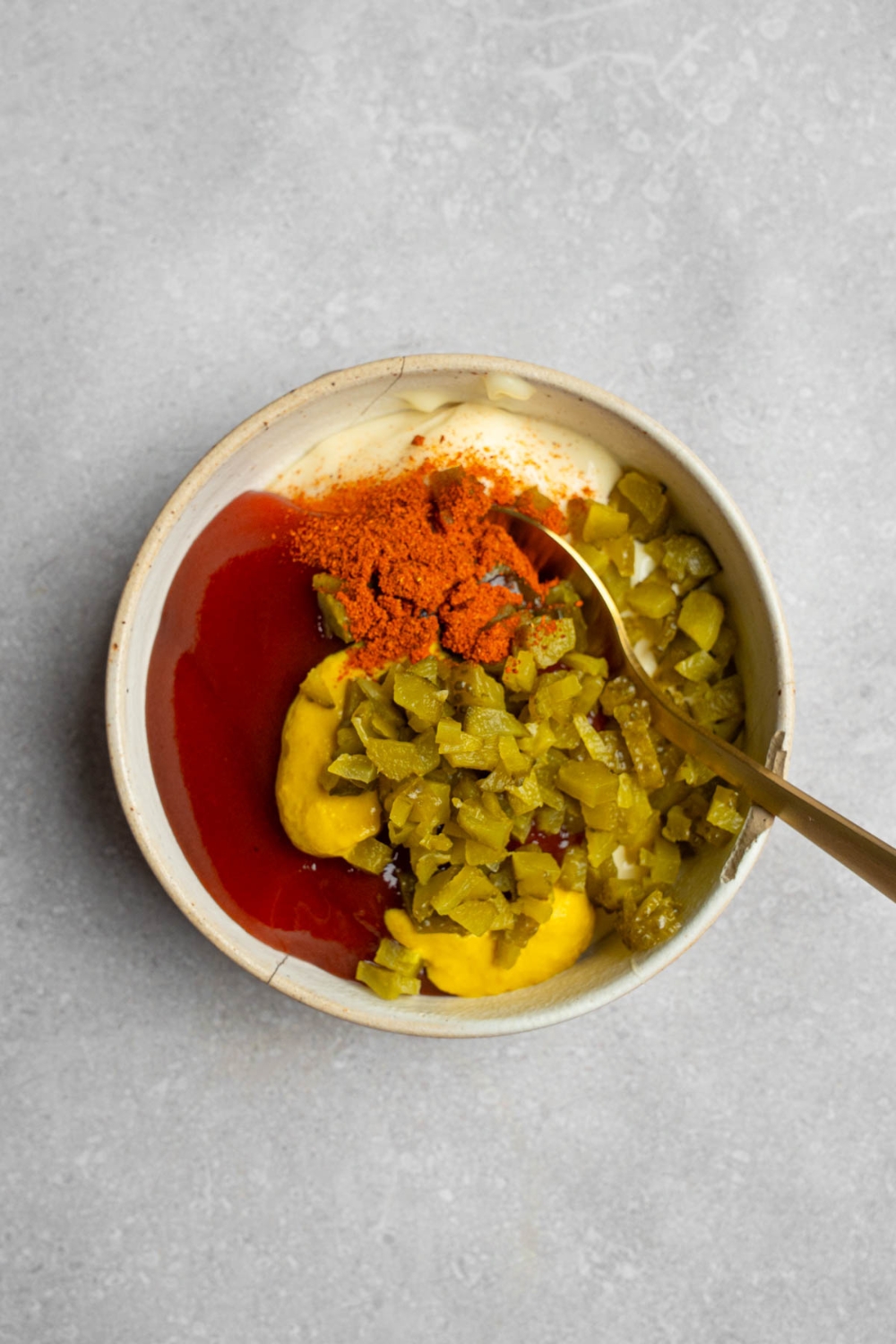 A white bowl with a spoon mixing ingredients to make Big Mac sauce including ketchup, mustard, relish, and seasonings. The bowl is on a white counter.