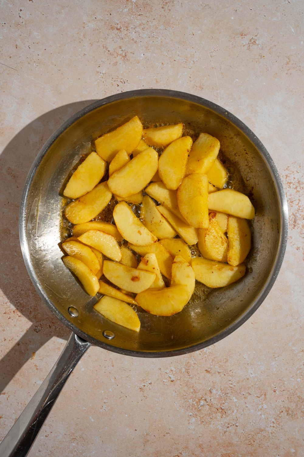 A frying pan with sliced apples cooking in melted butter. The pan is on a tan counter.