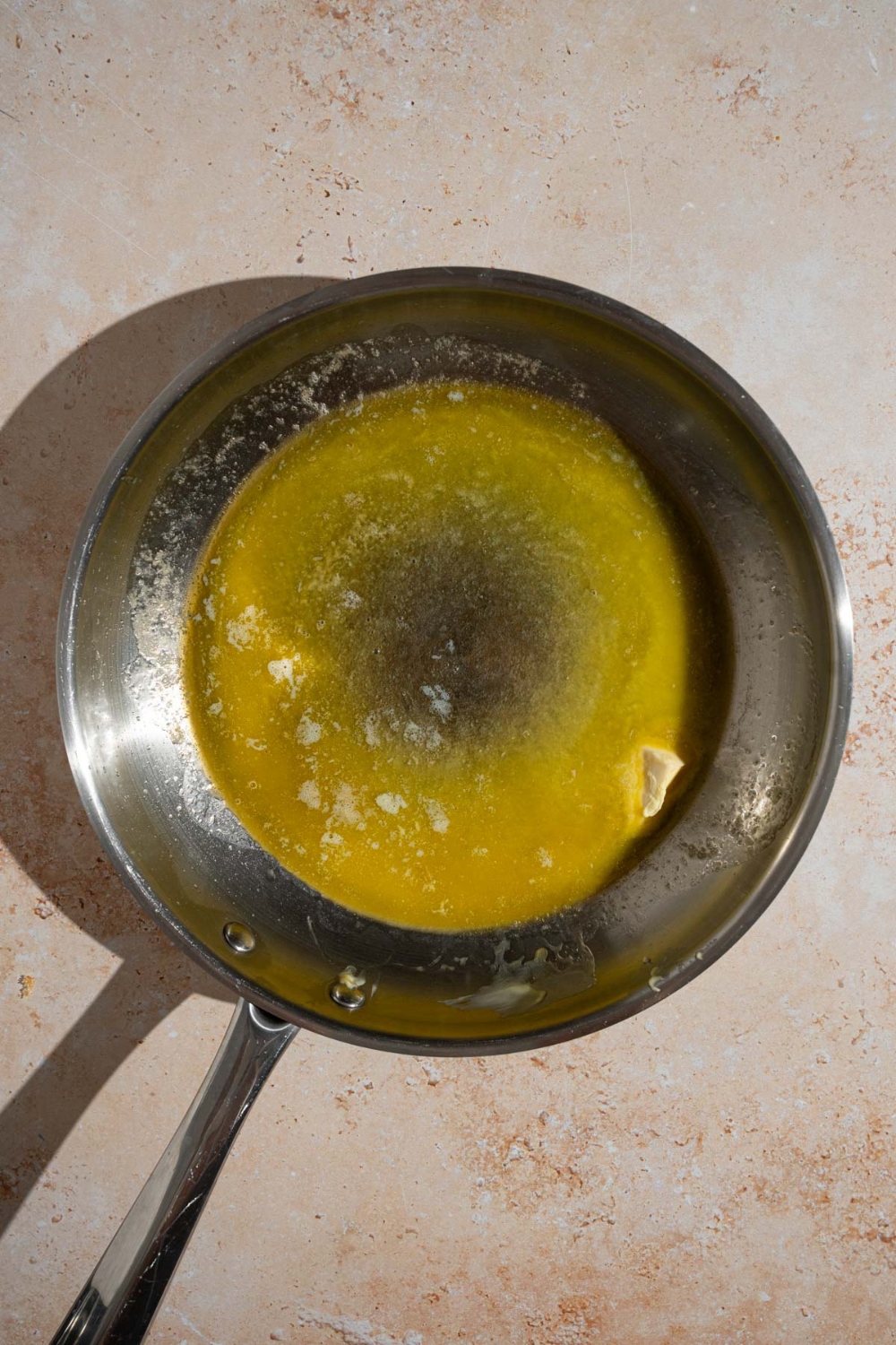 A frying pan with melted butter. The pan is on a tan counter.