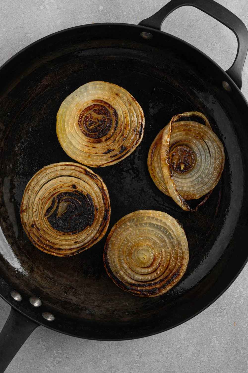 Four groups of sliced white onion slabs on a cast iron skillet. The skillet is on a white counter.