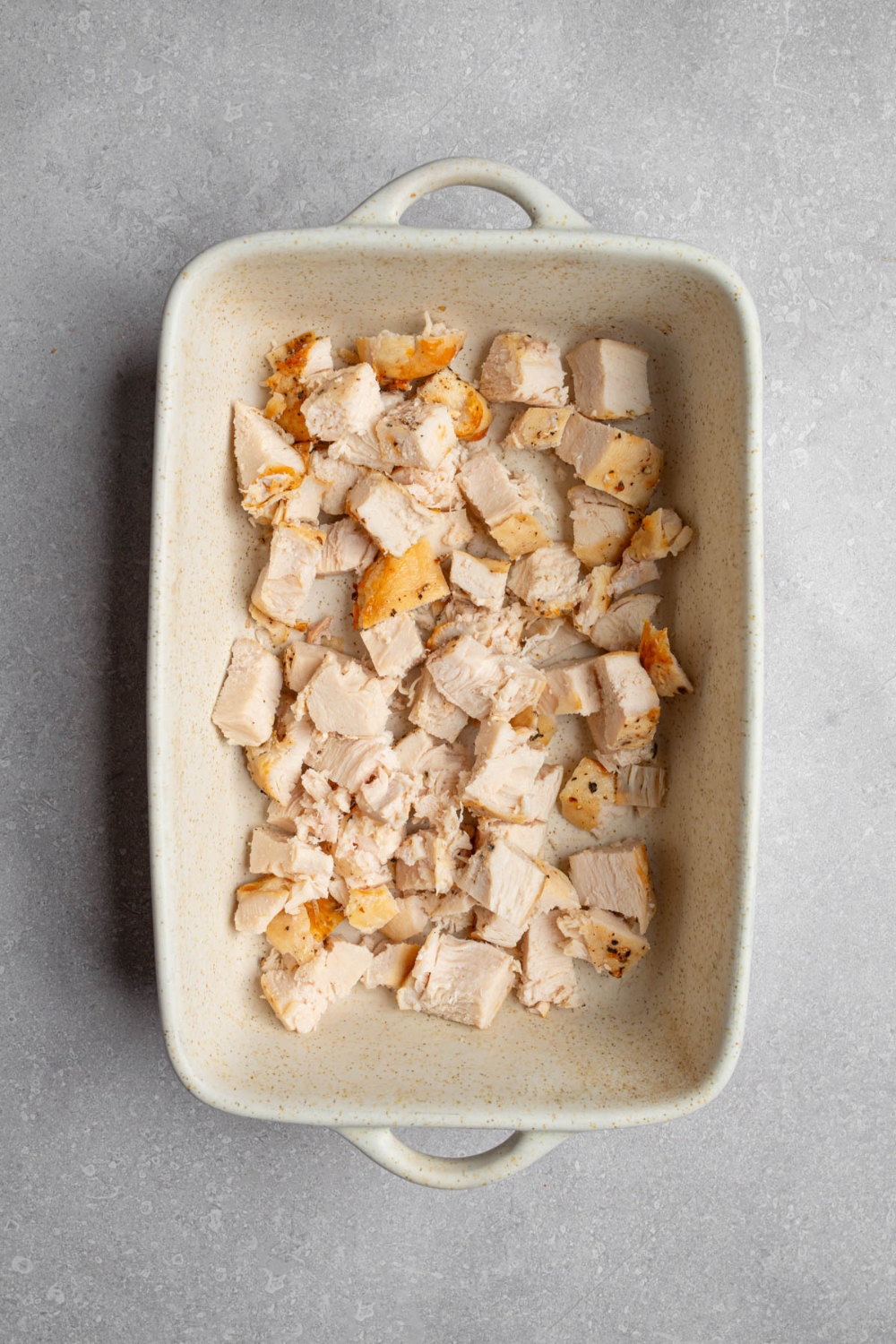 A baking dish with cubed chicken. The dish is on a white counter.