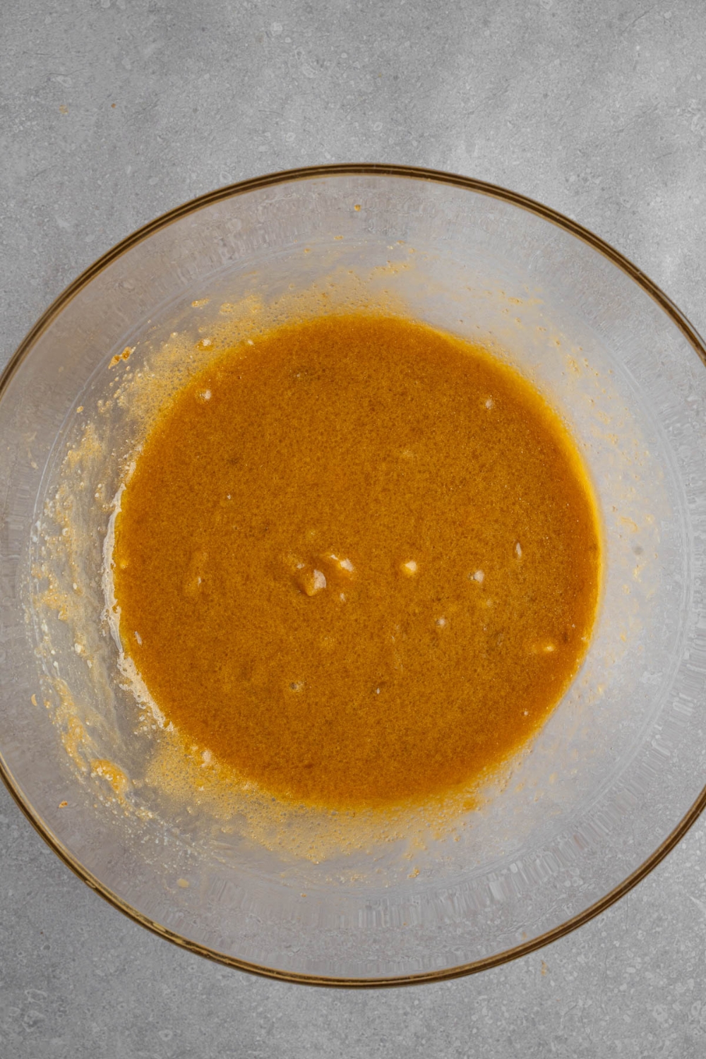 A glass bowl with a mixture of wet ingredients for banana bread cookies. The bowl is on a white counter.