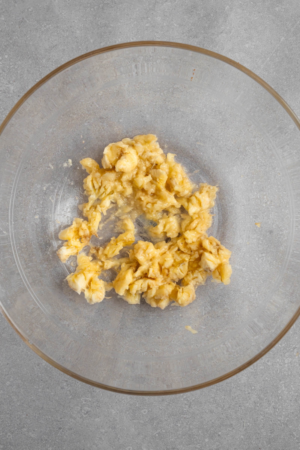 A glass bowl with mashed banana. The bowl is on a white counter.