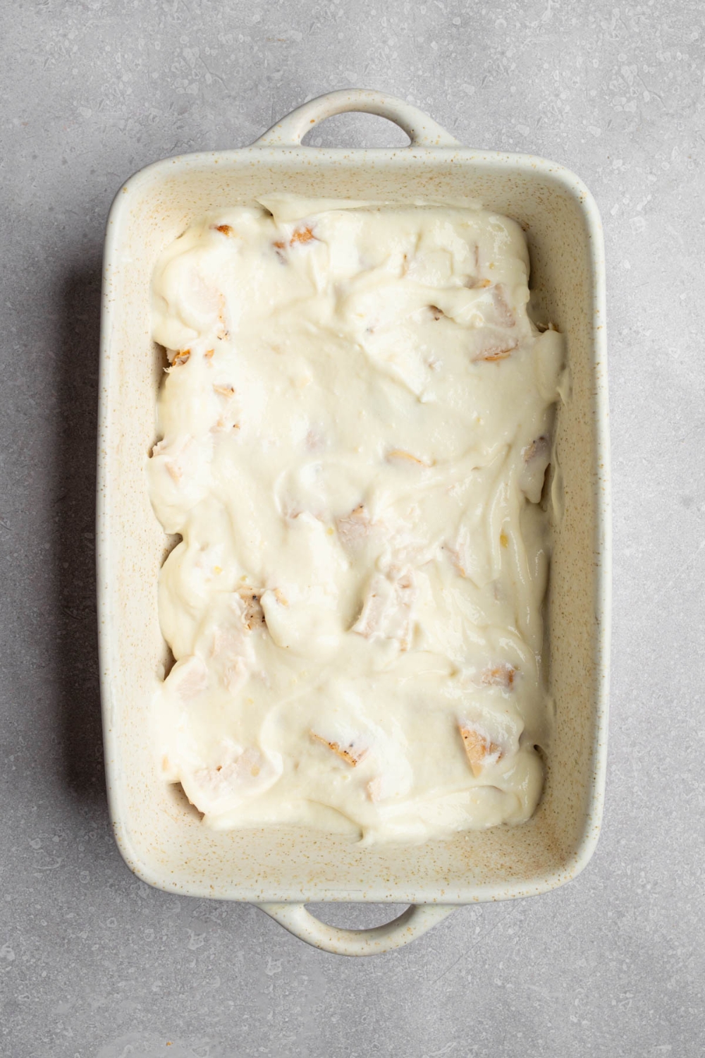 A baking dish with cubed chicken covered with a creamy cheese mixture. The dish is on a white counter.