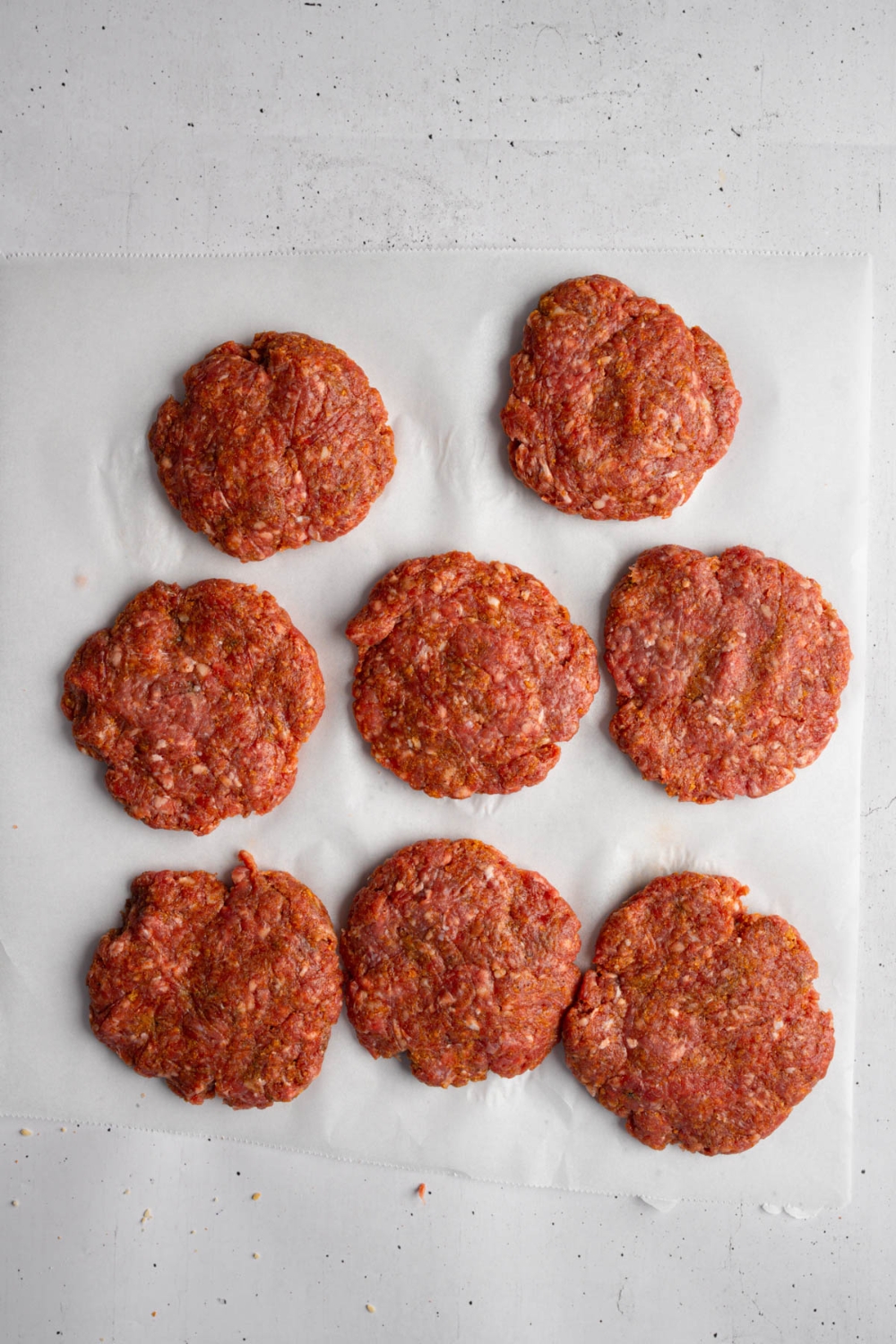 Several brisket patties on a piece of parchment paper. The parchment is on a white counter.