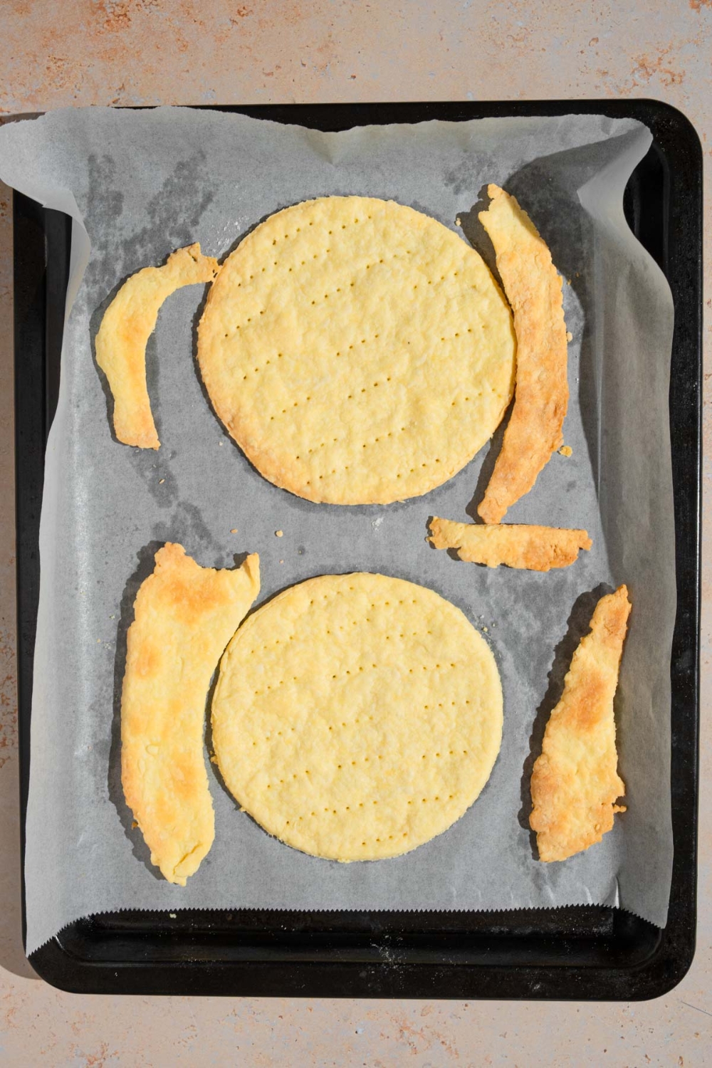 A baking sheet lined with parchment paper with two baked round pastry cuts. The sheet is on a tan counter.