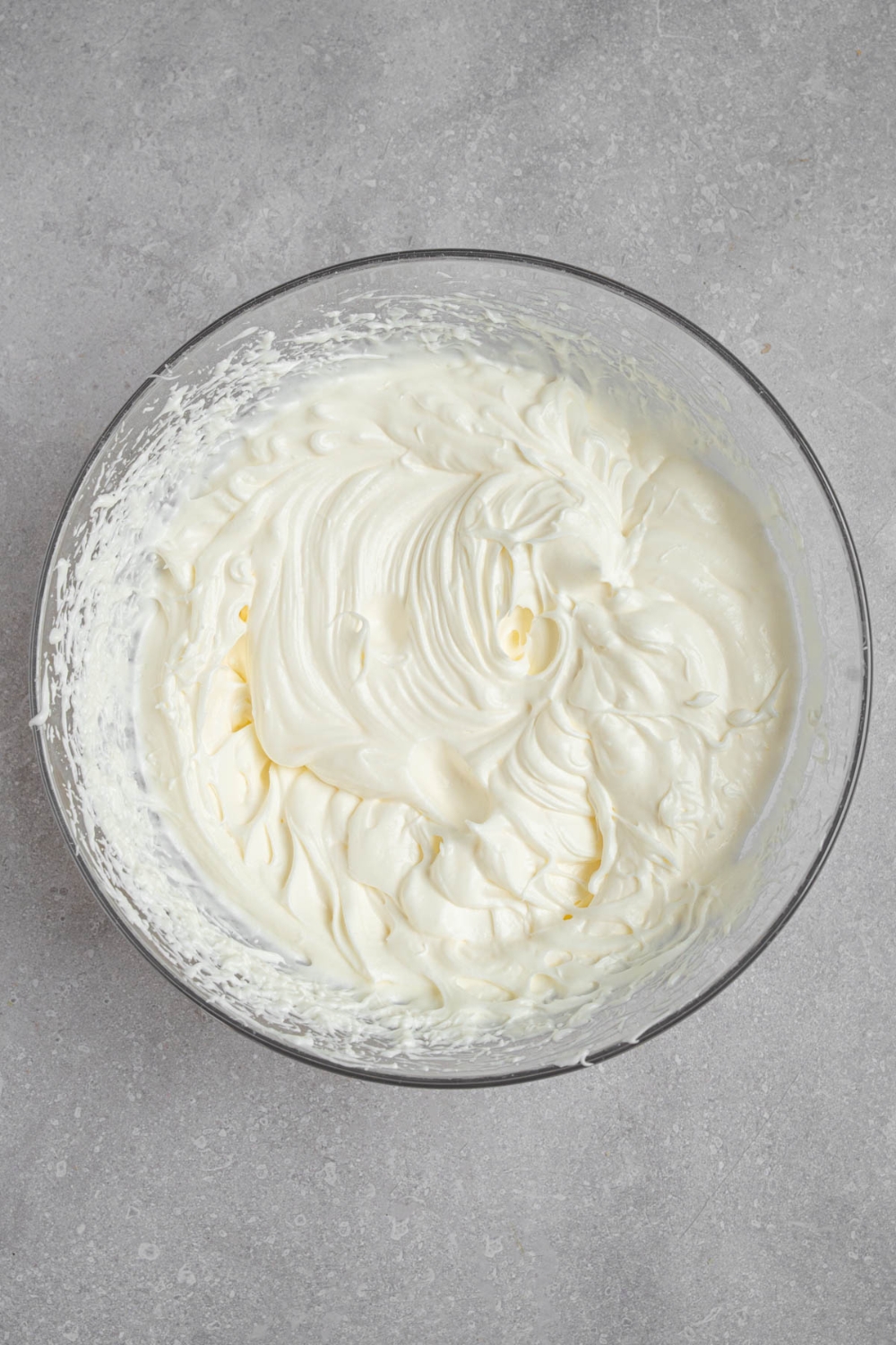 A glass bowl of whipped cream frosting. The bowl is on a white counter.