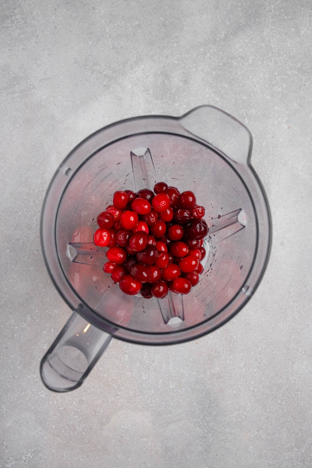 A glass blender with chokecherries. The blender is on a white counter.