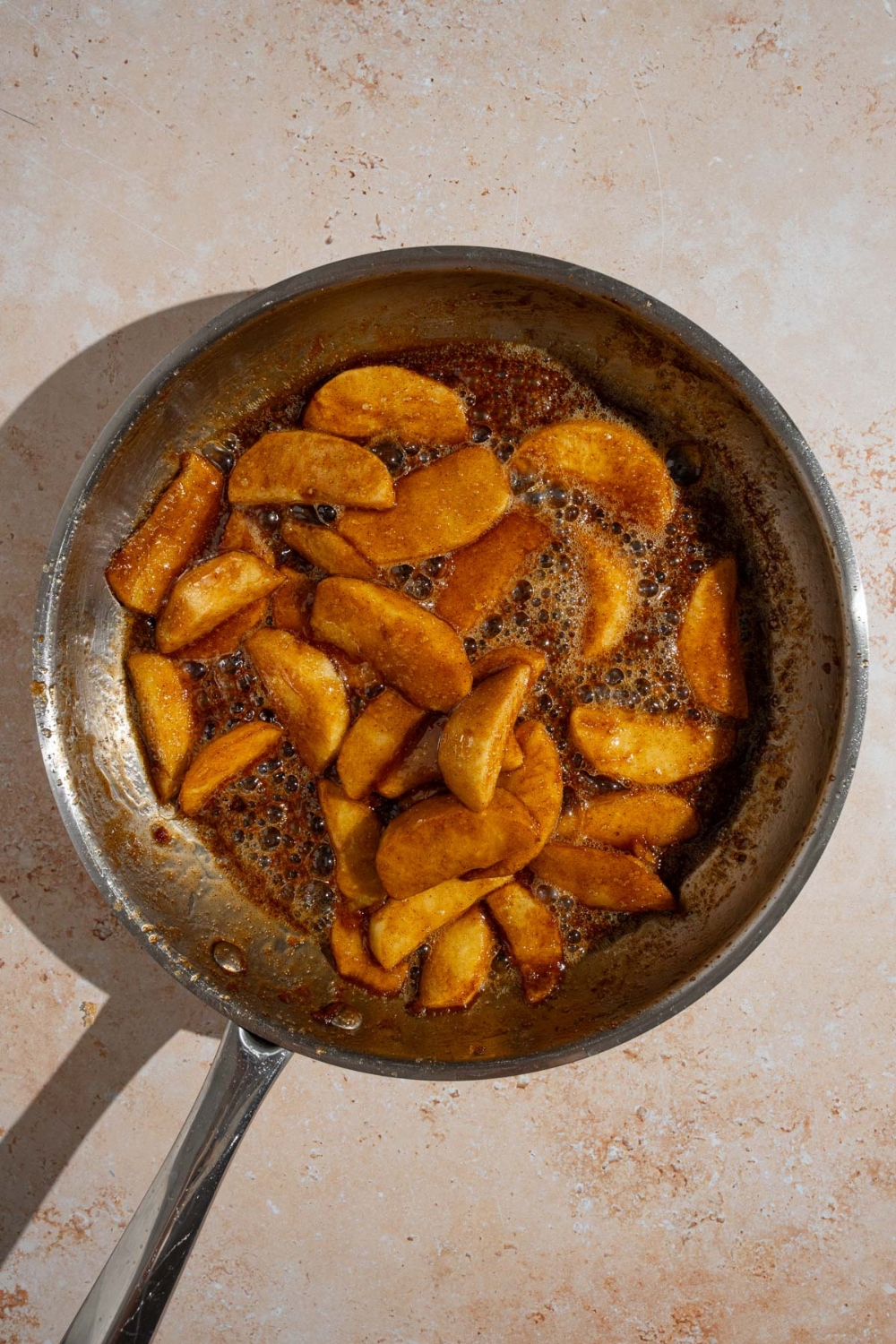 A frying pan with sliced apples cooking in butter and spices. The pan is on a tan counter.