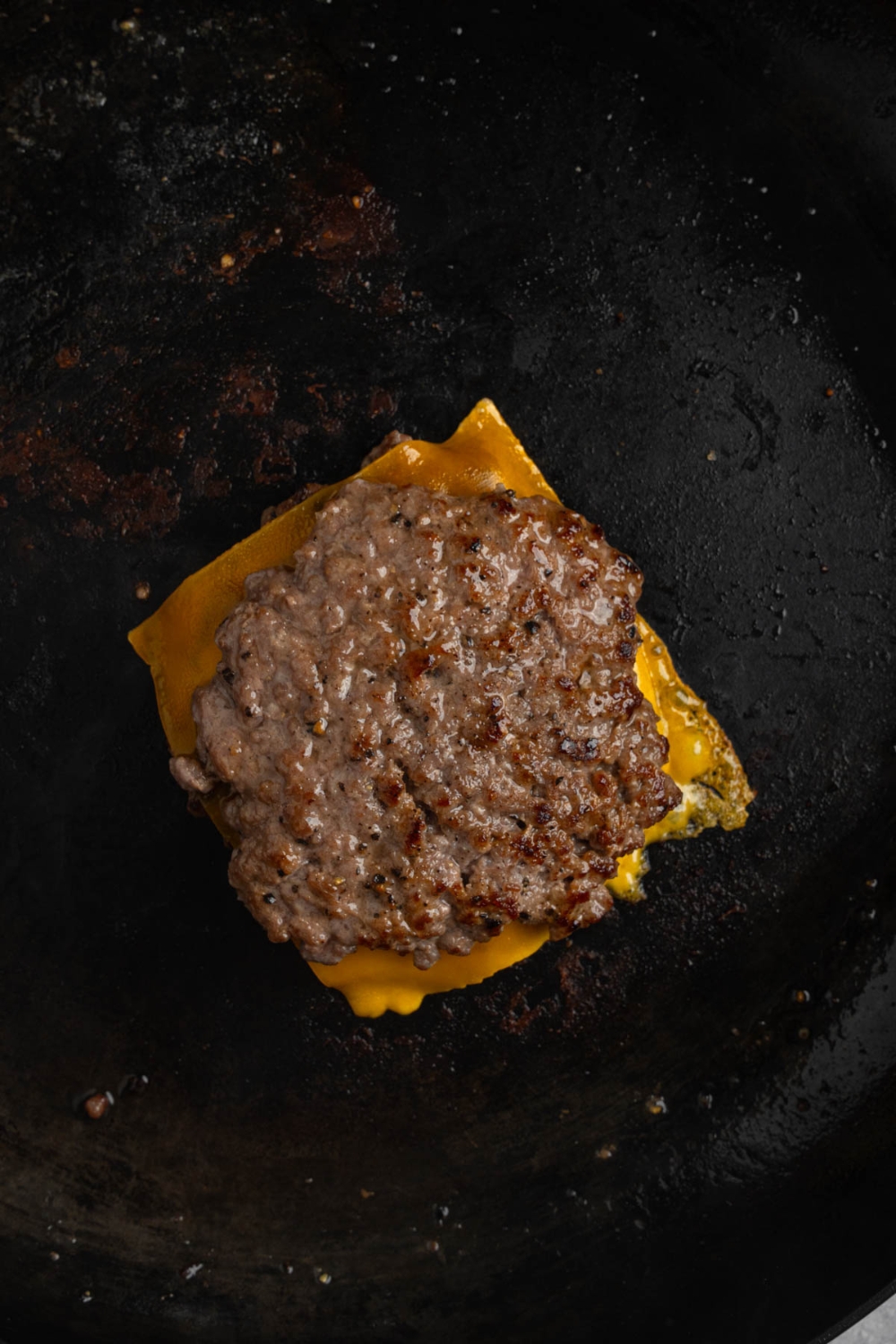 Two smashed patties layere with cheese on a cast iron skillet.