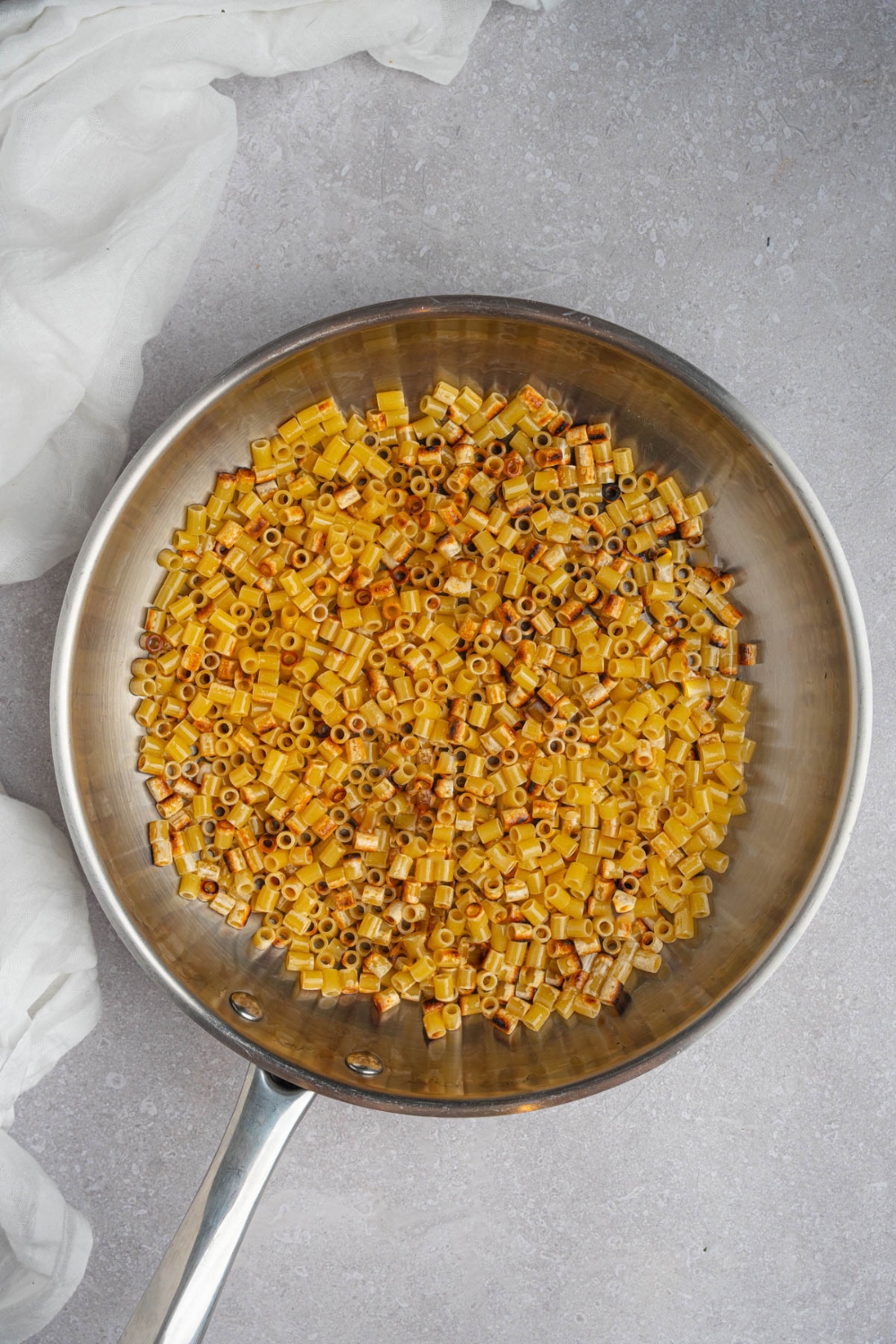 A skillet with browned ditalini pasta on a white counter with a white cloth napkin.