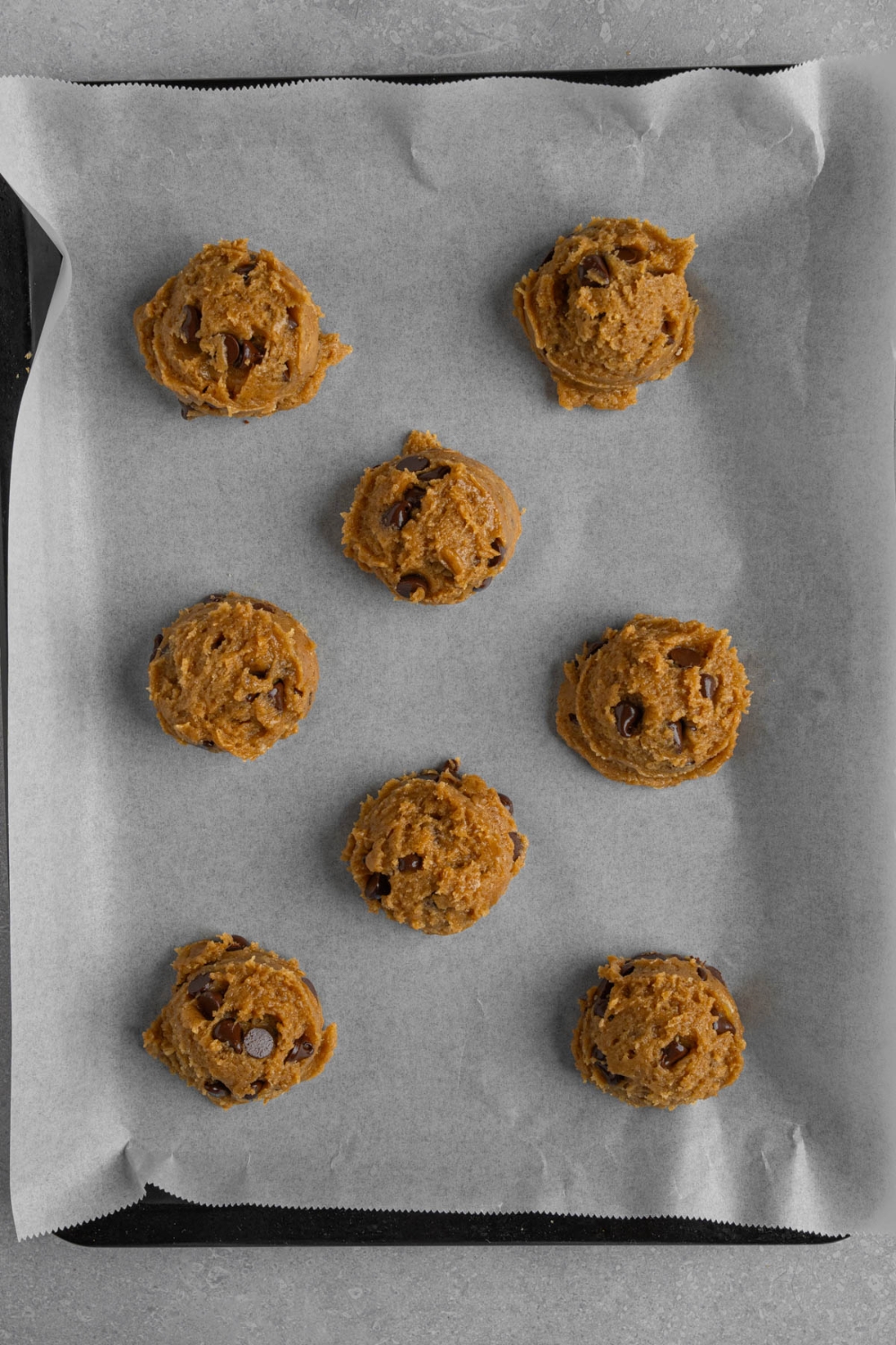 Eight banana bread cookie dough balls on a baking sheet lined with parchment paper.