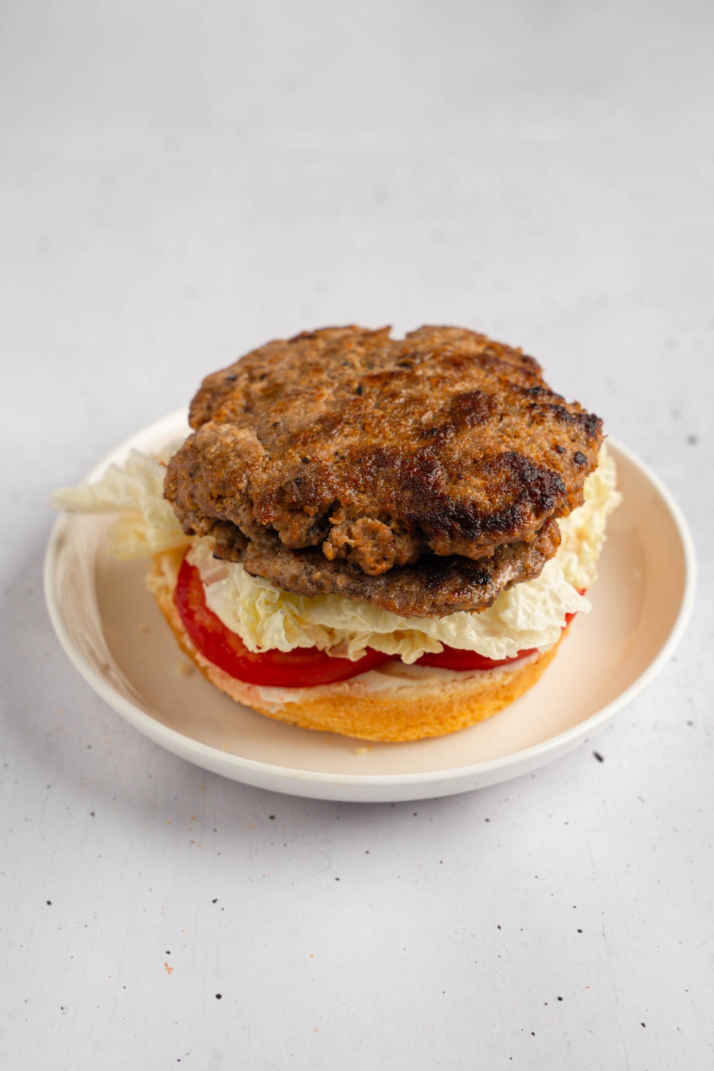 An open brisket burger with sliced tomato on a white plate. The plate is on a white counter.