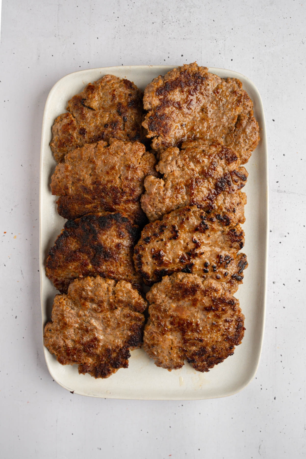 A white platter with several brisket patties. The platter is on a white counter.