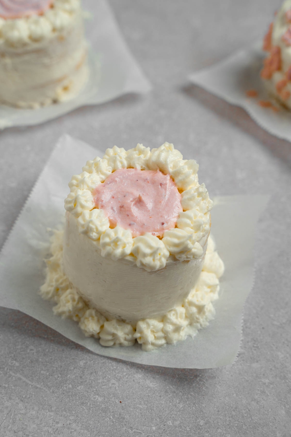 A vanilla lunch box cake with purple icing. The cake is on a piece of parchment paper on a white counter with other cakes.