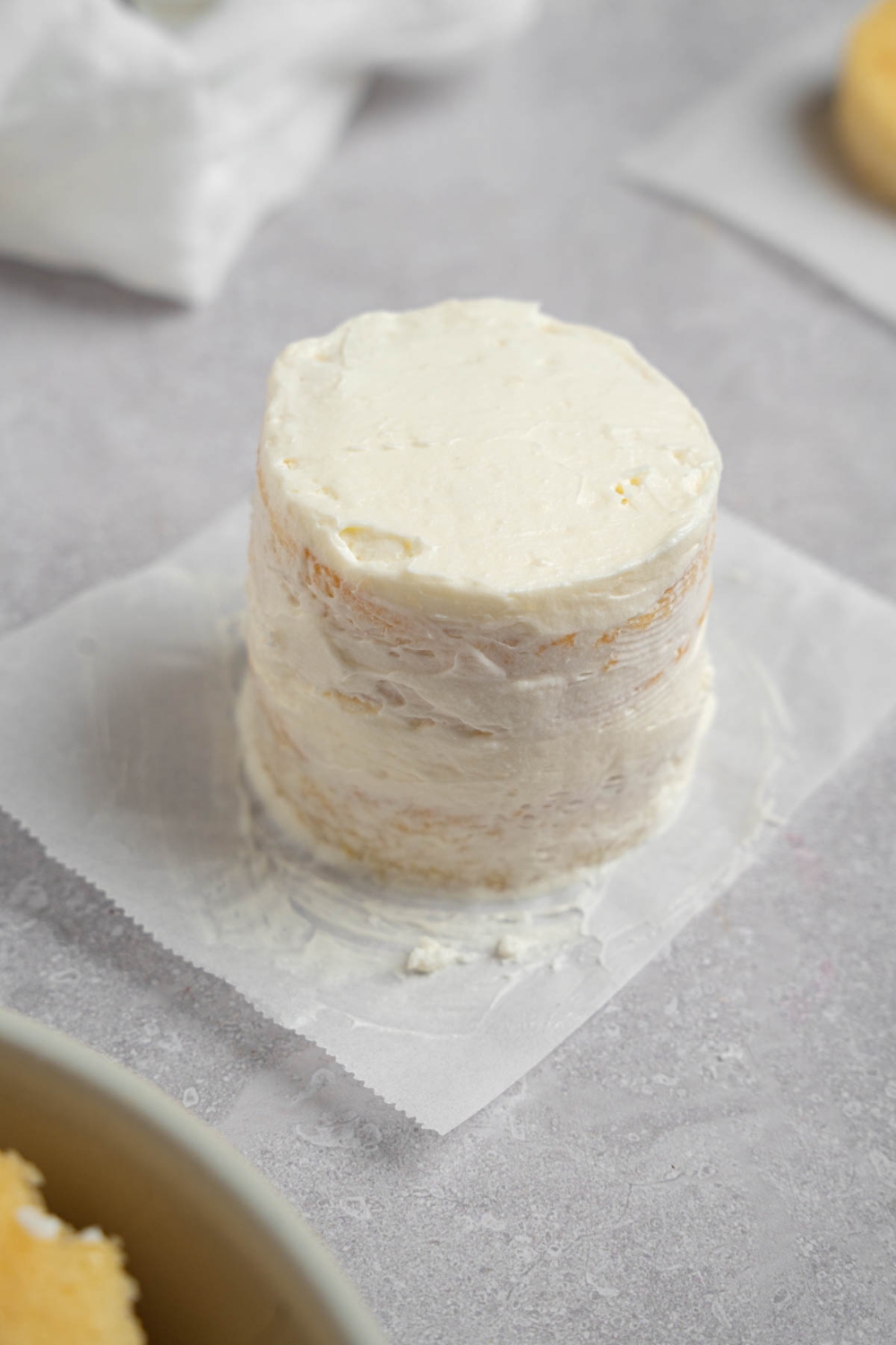 A vanilla lunch box cake coated in whipped cream frosting. The cake is on a piece of parchment paper on a white counter.