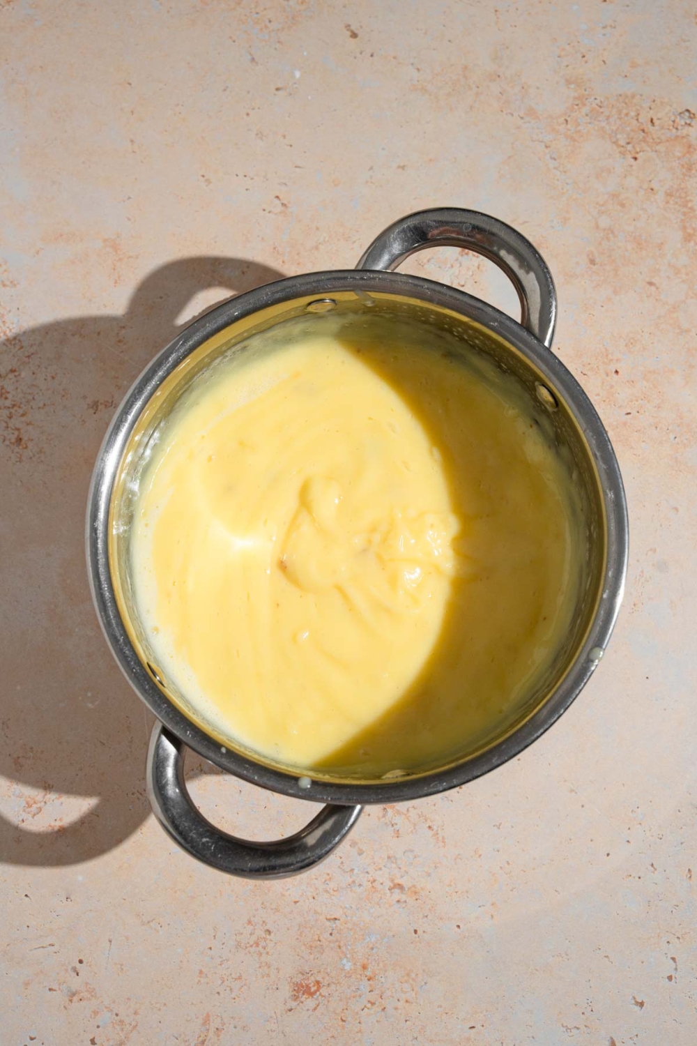 A pot with cooked pastry cream. The pot is on a tan counter.