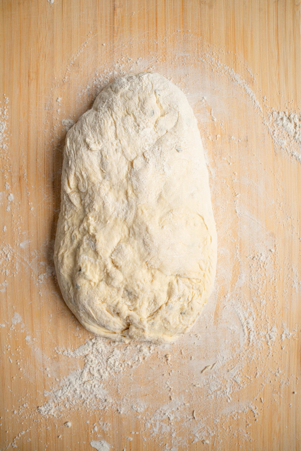 A wooden board dusted with flour with garlic rosemary bread dough shaped into a loaf.