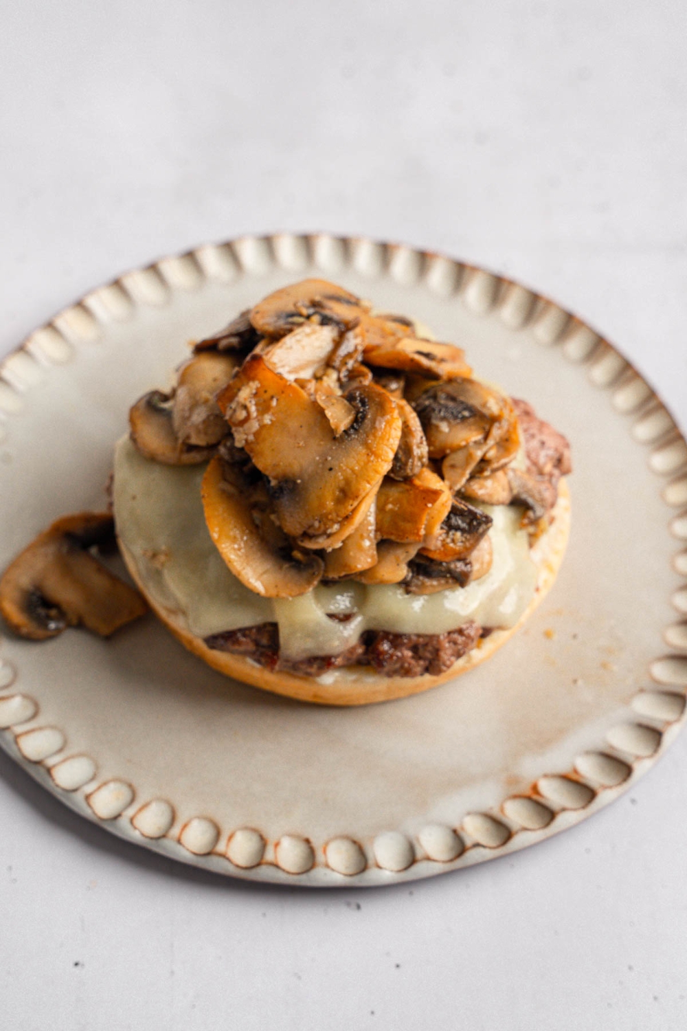 An open mushroom swiss burger on a ceramic plate. The plate is on a white counter.