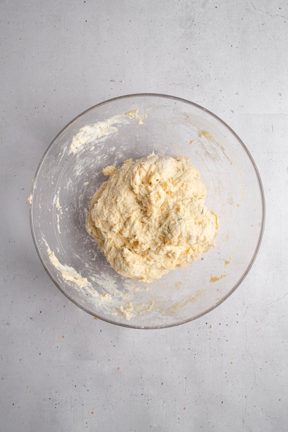 A glass bowl with a ball of garlic rosemary bread dough. The bowl is on a white counter.