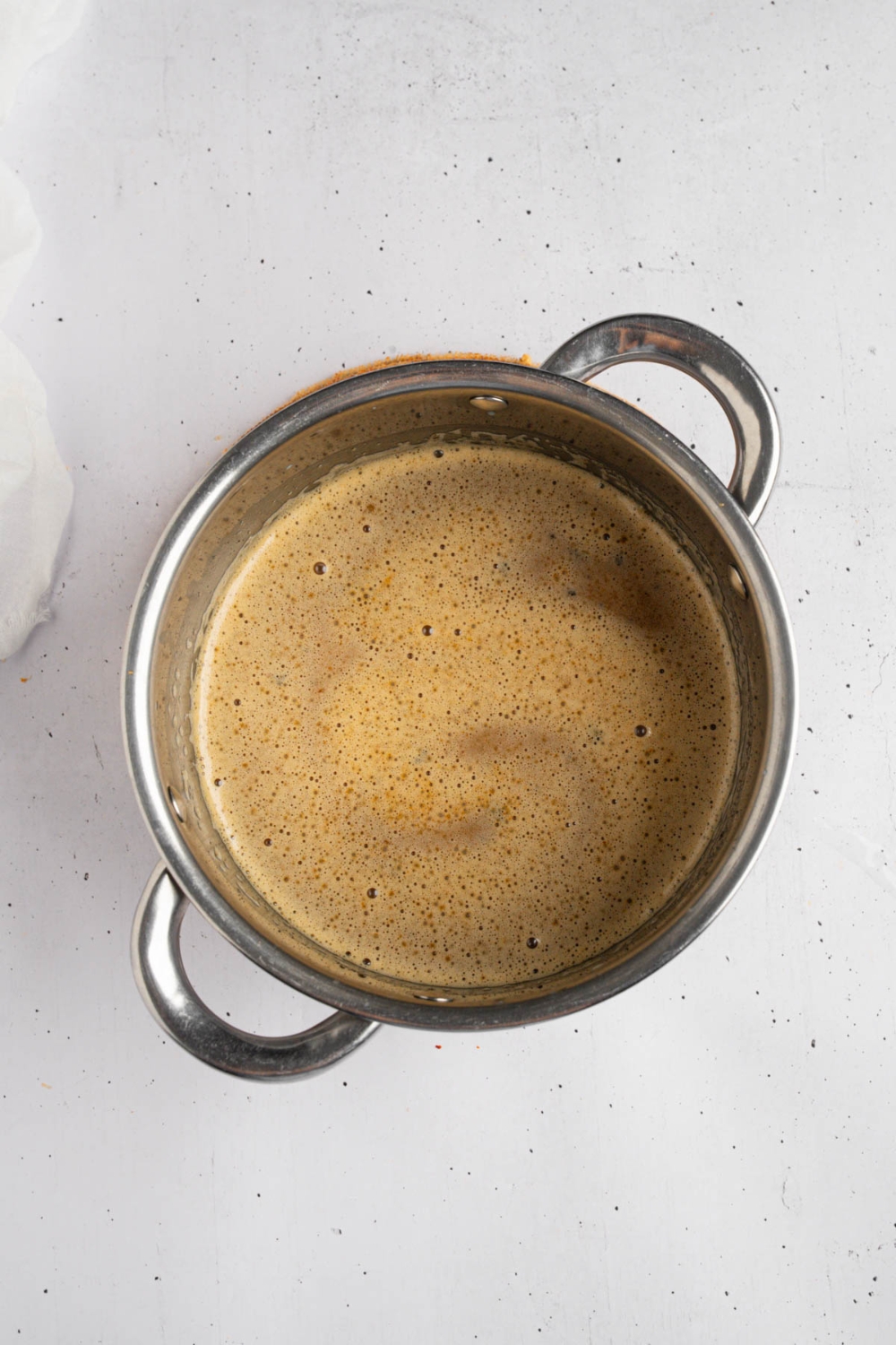 A pot with butter, sugar, condensed milk, milk, and vanilla cooking. The pot is on a white counter.