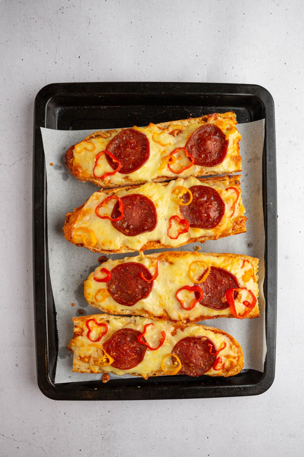 A lined baking sheet with pieces of baked garlic bread pizza. The baking sheet is on a white counter.