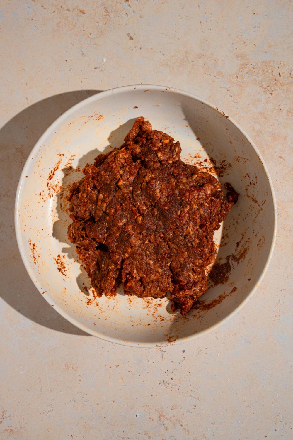 A white bowl with ground beef tossed in spices. The bowl is on a tan counter.