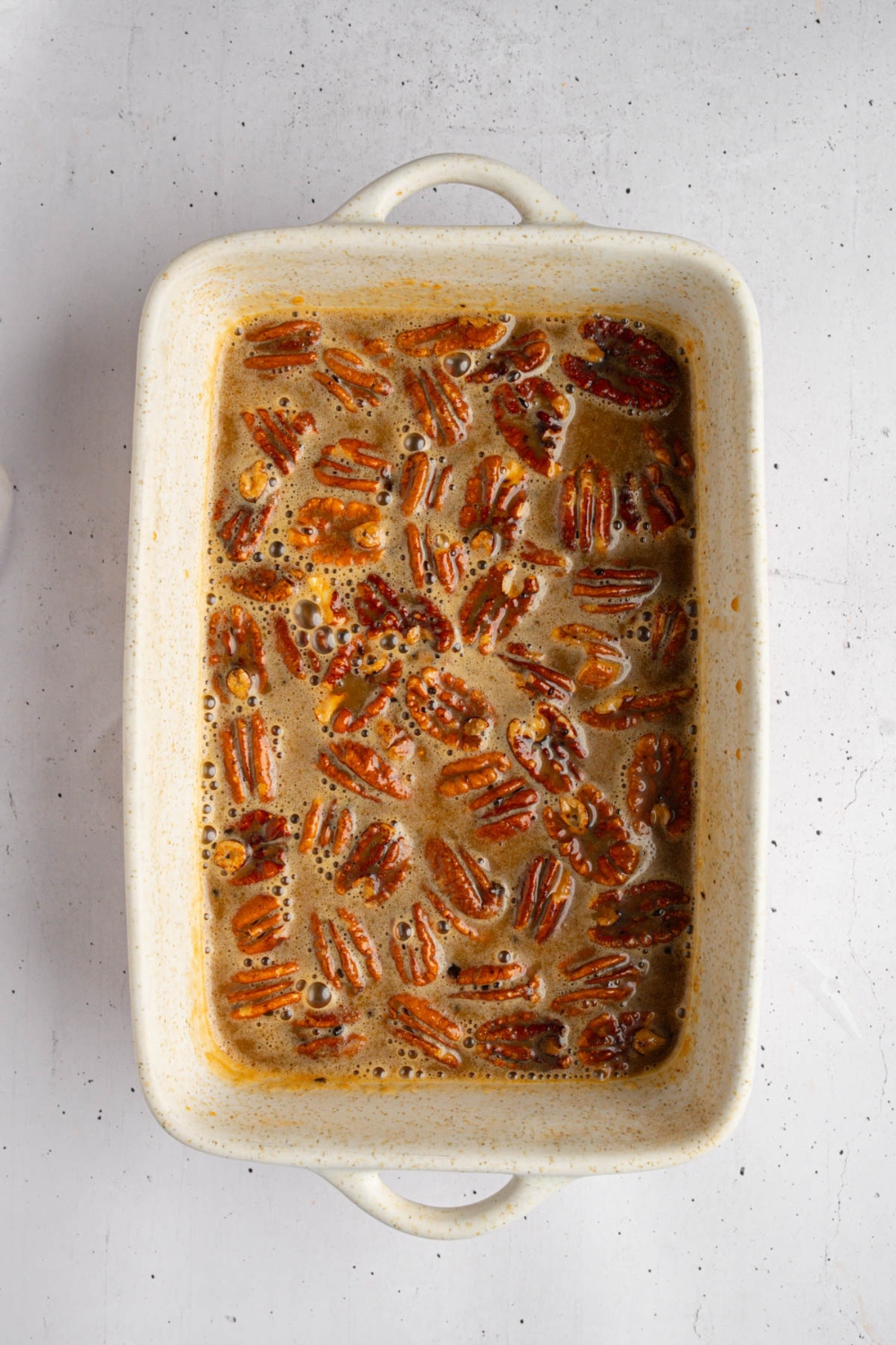 A baking dish with pecans in caramel sauce. The dish is on a white counter.