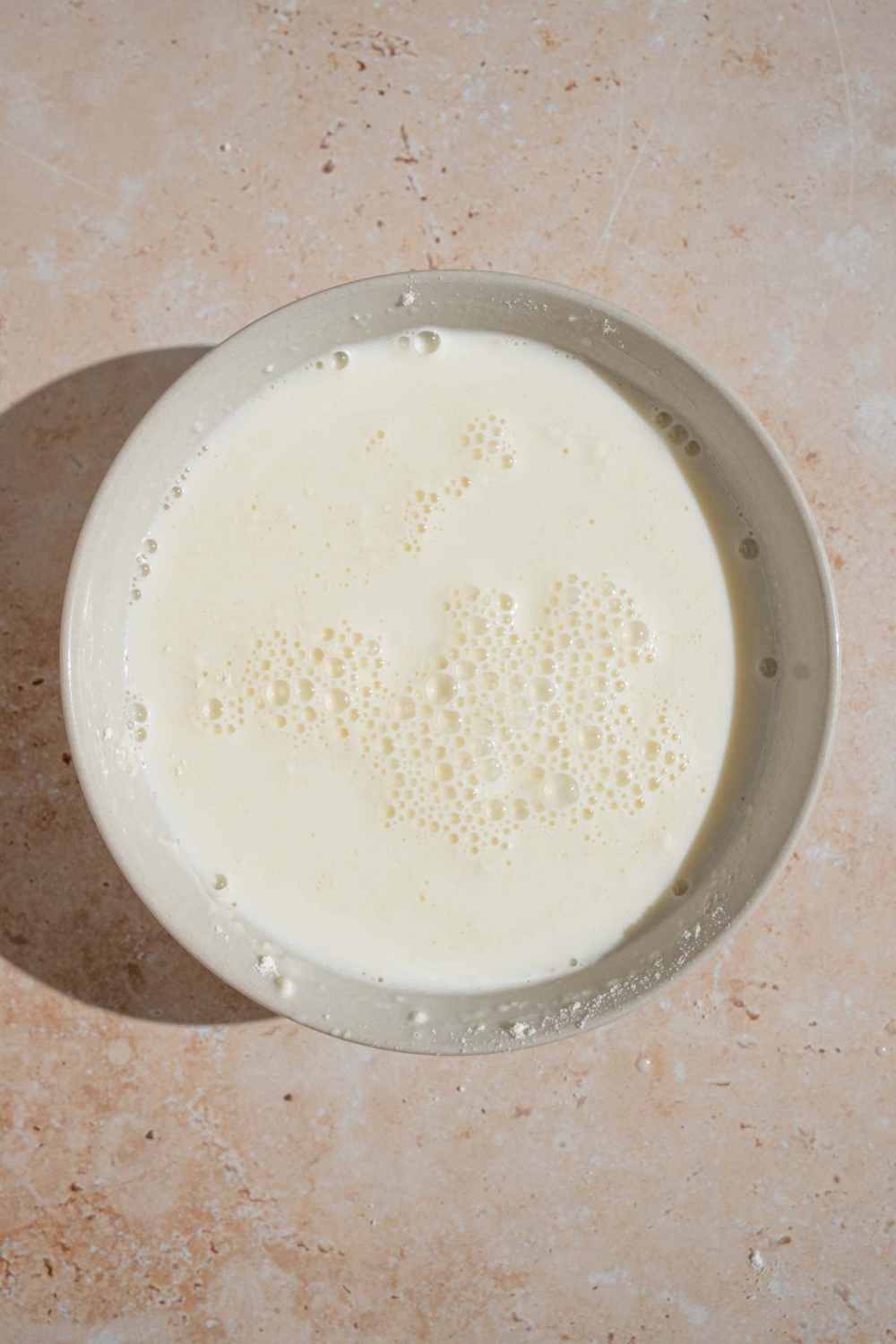 A bowl with a milk and flour slurry. The bowl is on a tan counter.