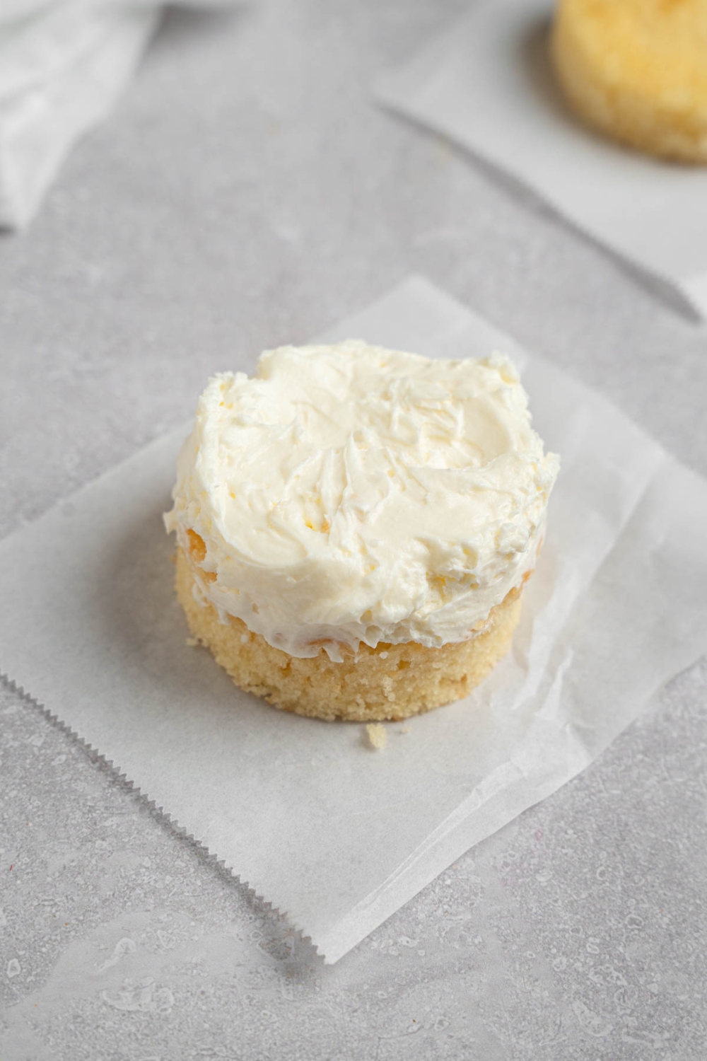 A single layer of vanilla lunch box cake with whipped cream frosting. The cake is on a piece of parchment paper on a white counter.