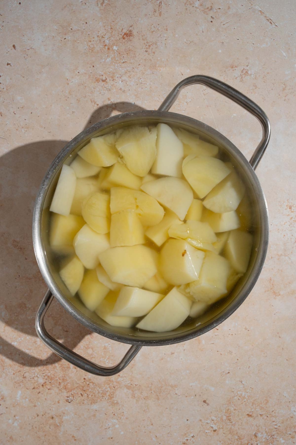 A pot with cut potatoes in water. The pot is on a tan counter.