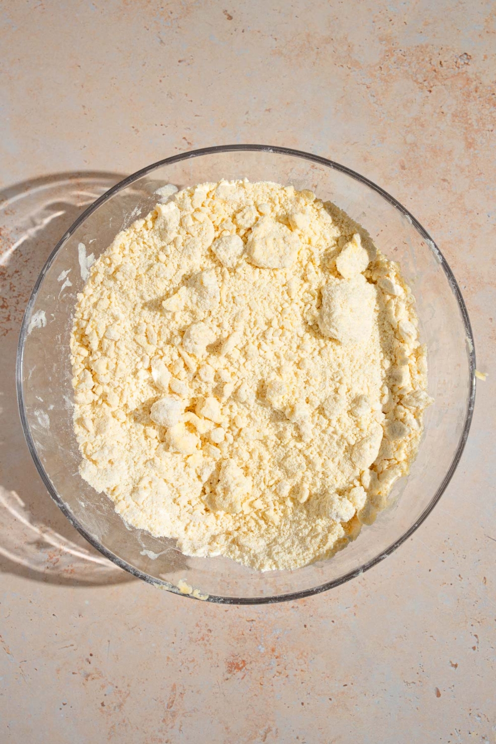 A glass bowl with a flour, butter, and salt mixture. The bowl is on a tan counter.