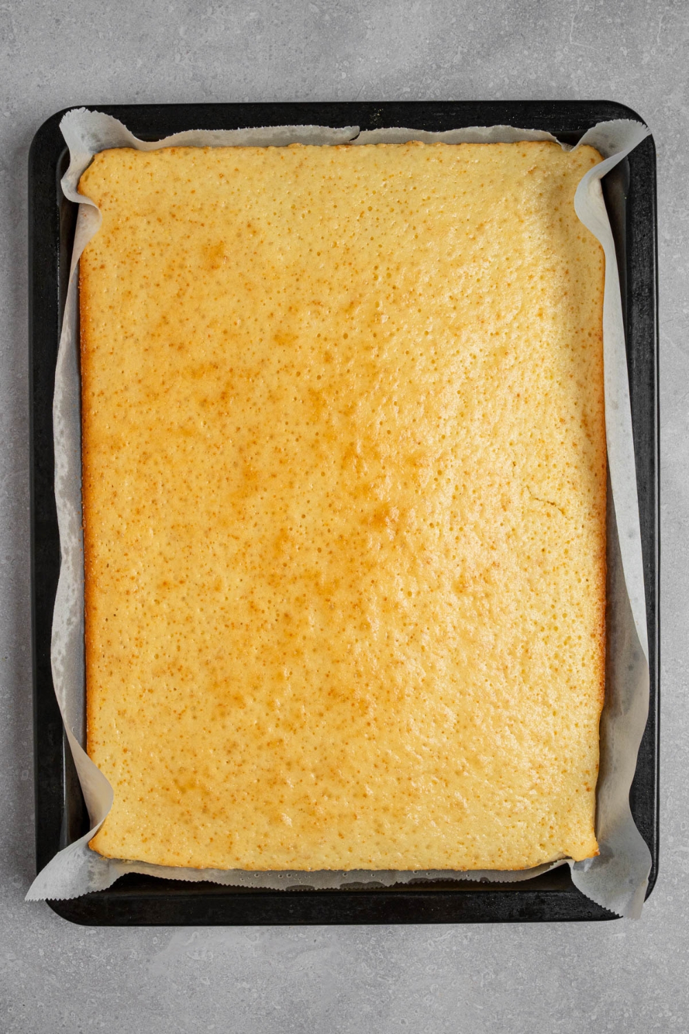 A cake pan lined with parchment paper with baked vanilla cake. The pan is on a white counter.