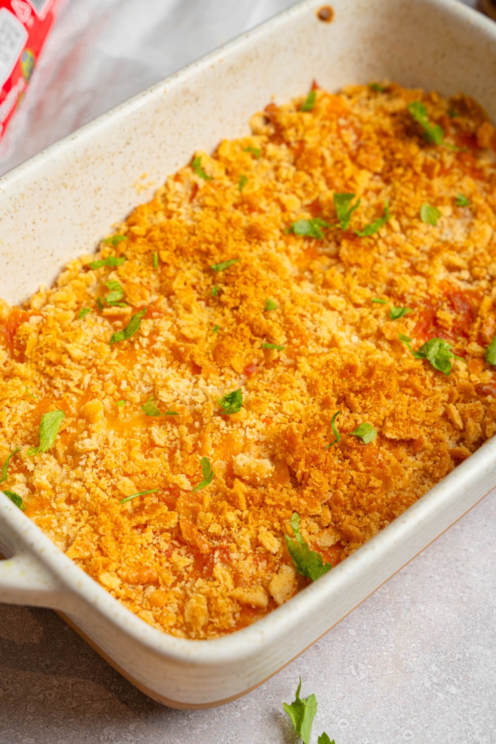A baking dish with Neiman Marcus chicken casserole garnished with fresh parsley. The dish is on a white counter.