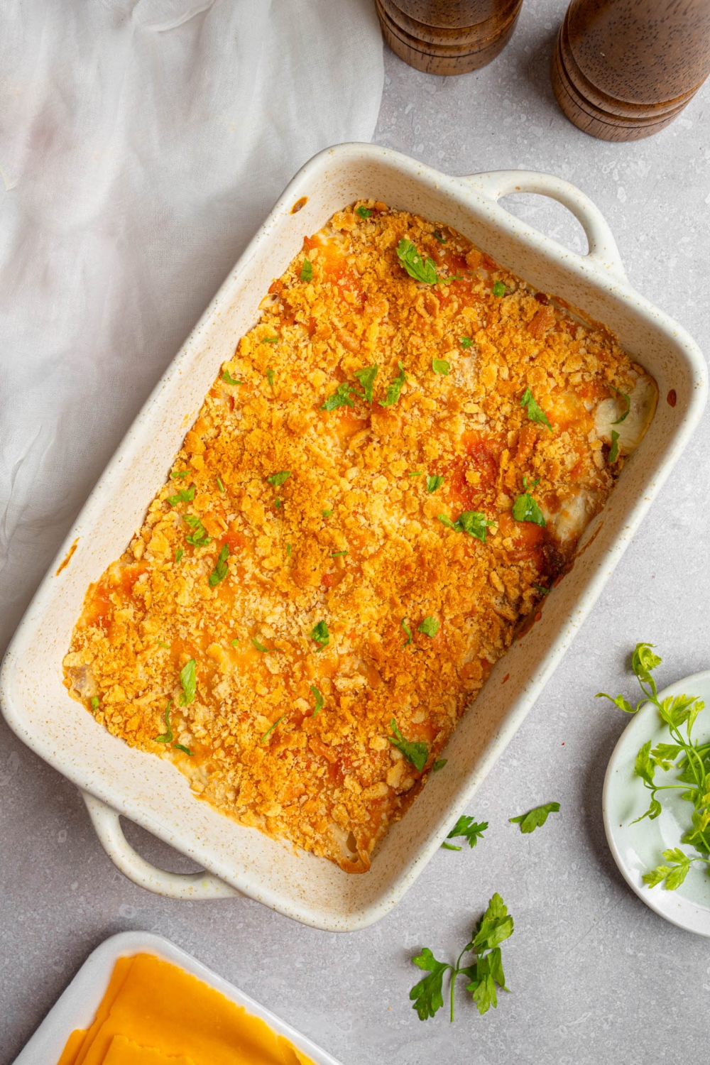 A baking dish with Neiman Marcus chicken casserole garnished with fresh parsley. The dish is on a white counter with a small plate of garnishes.