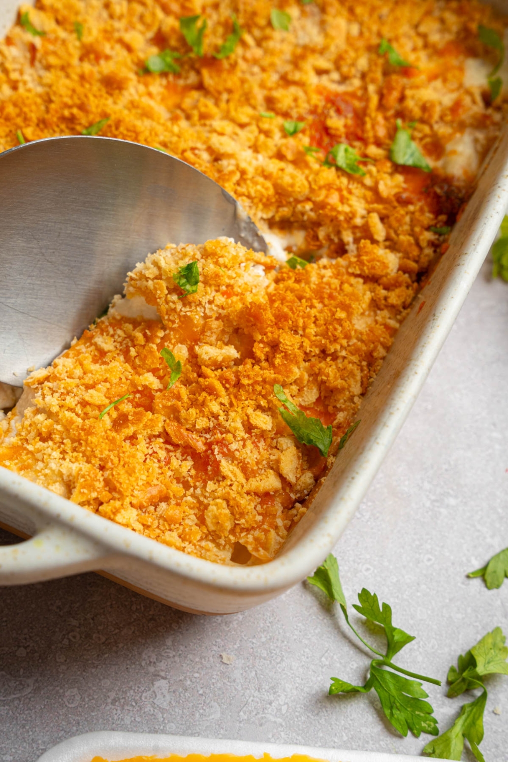 A baking dish with Neiman Marcus chicken casserole garnished with fresh parsley. There is a spoon taking a bite of casserole. The dish is on a white counter.