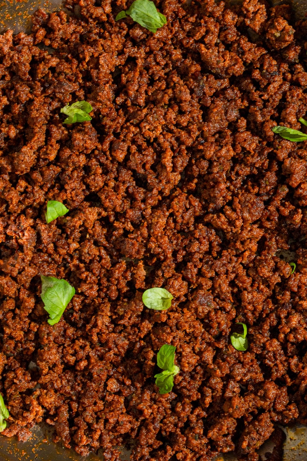 A close up of ground beef chorizo garnished with fresh basil.
