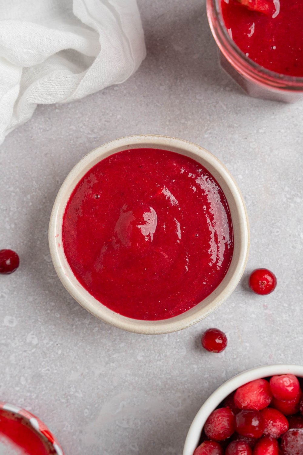 A small ramekin with chokecherry pudding. The ramekin is on a white counter with a glass jar of pudding and white bowl with chokecherries.