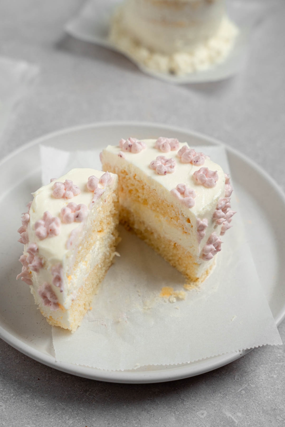 A vanilla lunch box cake with dotted purple icing sliced in half on a white plate The plate is on a white counter with another cake.
