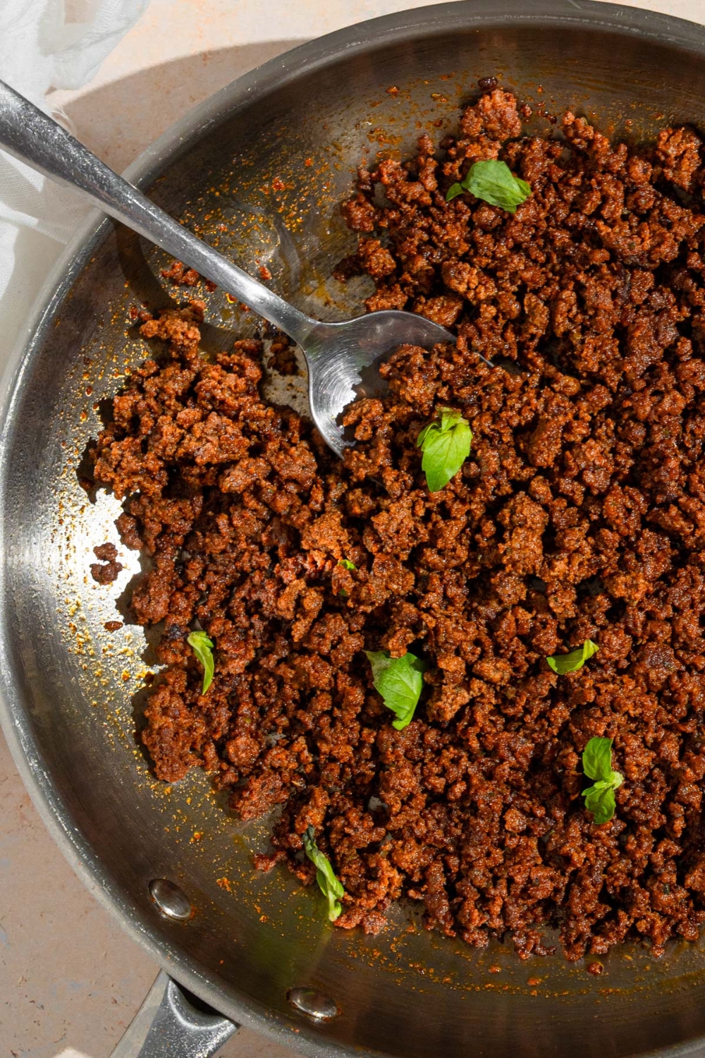 A skillet with cooked ground beef chorizo garnished with fresh basil. A fork is in the chorizo.