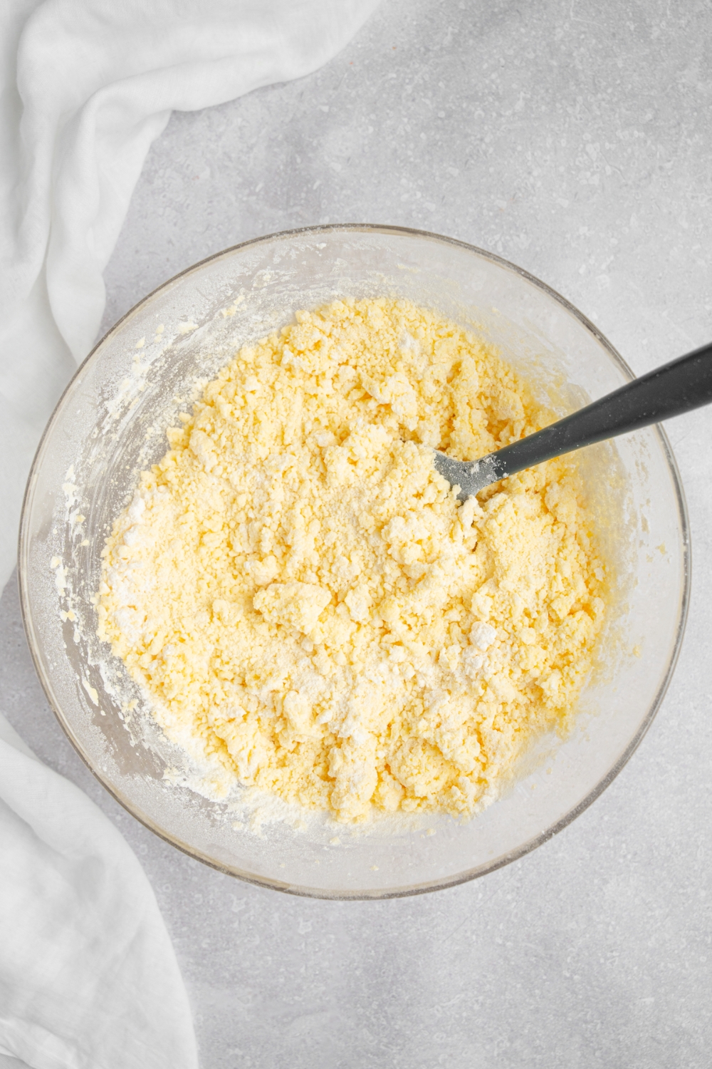 A crumbly mixed tres leches cake batter in a glass bowl on a grey counter.