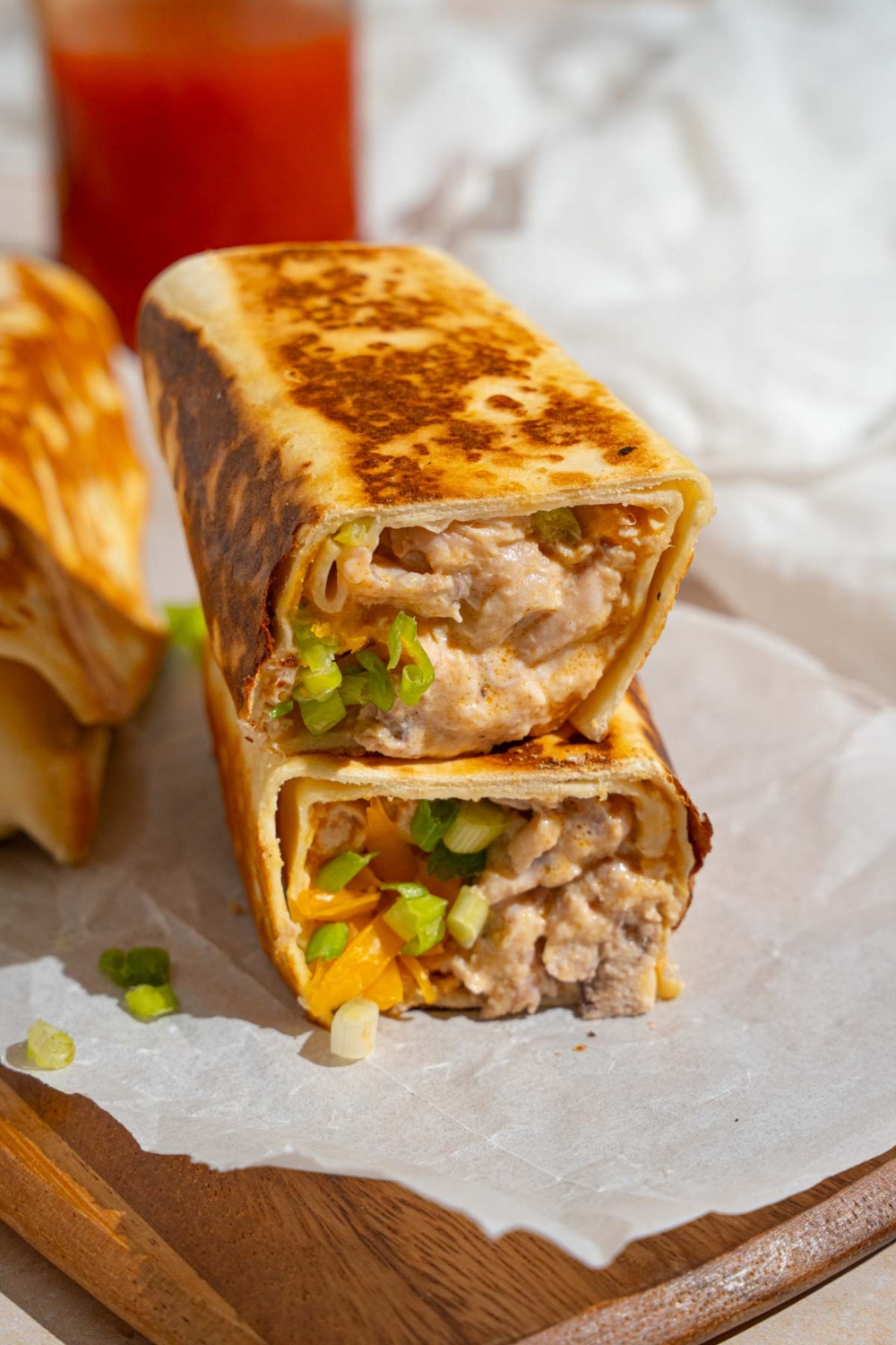 A cheesy garlic chicken wrap sliced in half on a wooden board lined with parchment paper. There is an additional wrap on the board.