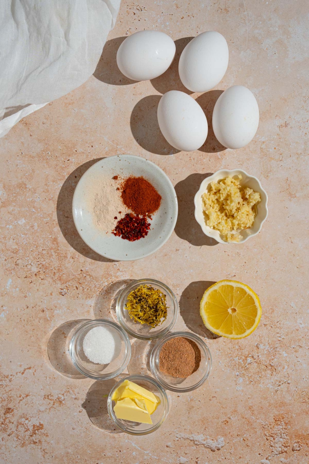 An overhead shot of several bowls in various sizes containing ingredients to make cajun boiled eggs including garlic, butter, eggs, sugar, and seasonings.