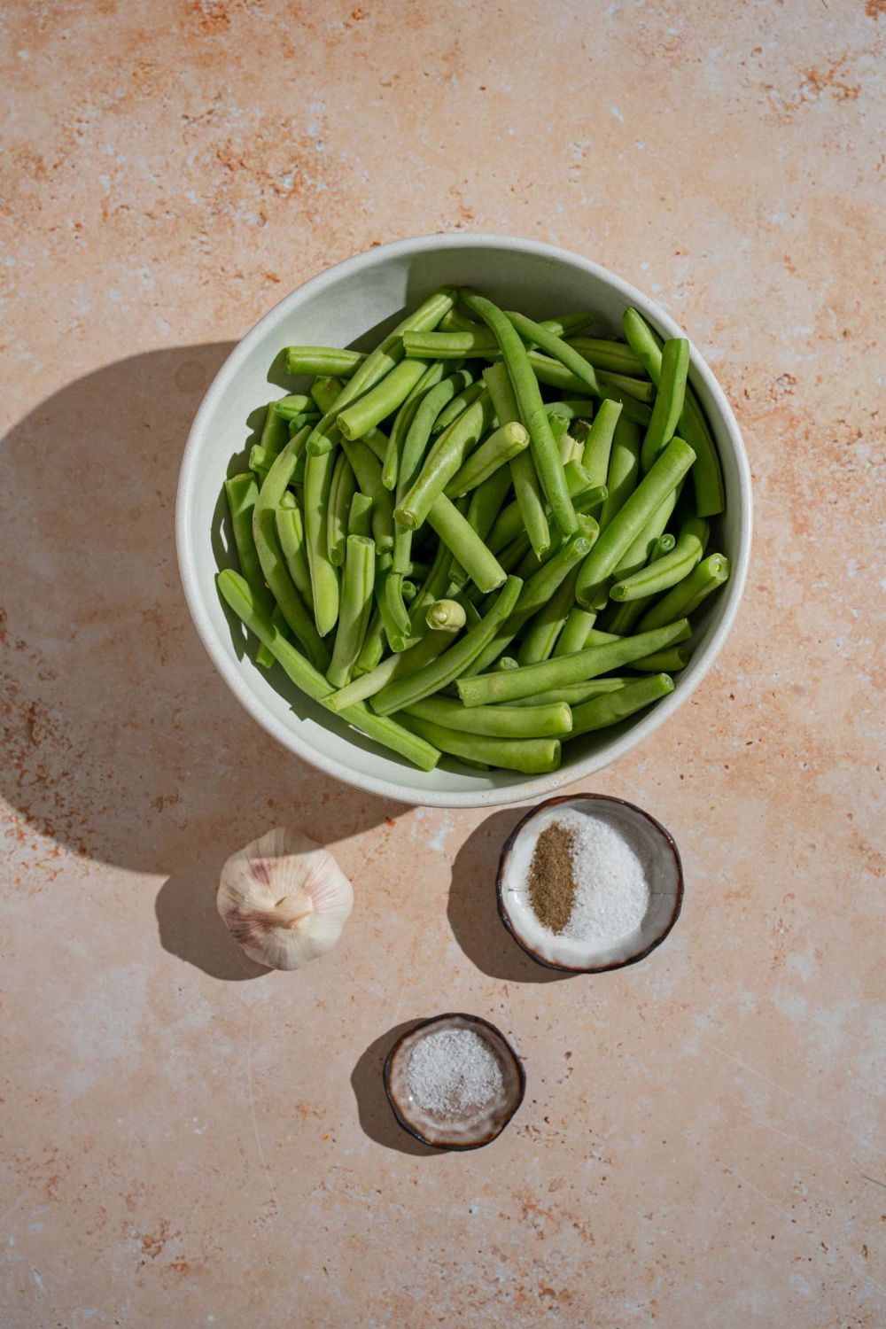 An overhead shot of several bowls in various sizes containing ingredients to make Din Tai Fung green beans including trimmed green beans, garlic, salt, pepper, and MSG.