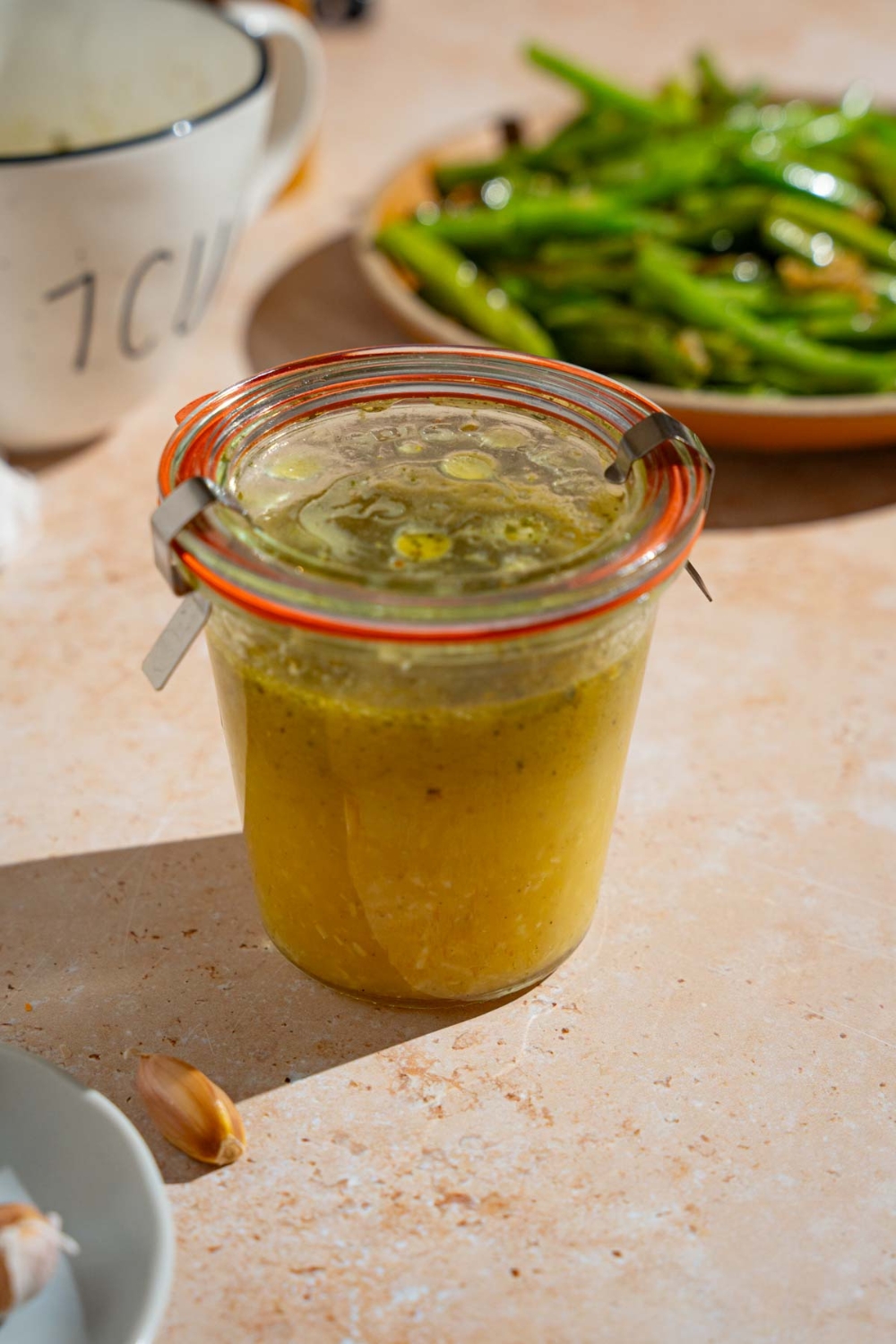 A sealed jar of copycat Texas Roadhouse italian dressing. The dressing is on a tan counter with a plate of green beans.