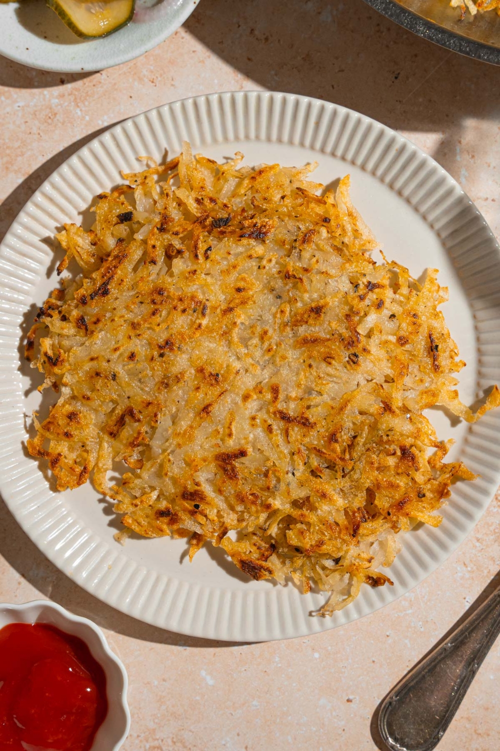 A white plate with copycat Waffle House hash browns. The plate is on a tan counter with a side of ketchup.